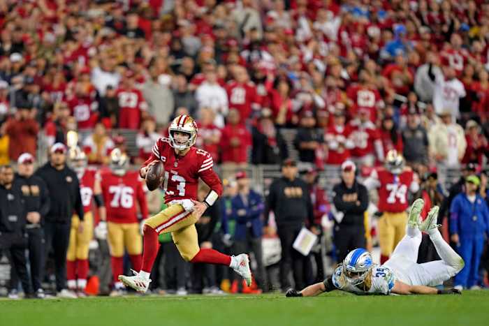 Brock Purdy runs with the ball as a Lions defender lays on the ground behind him